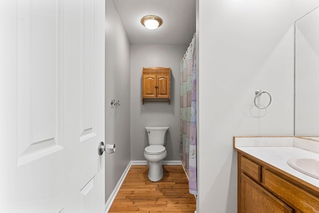 bathroom with wood finished floors, vanity, toilet, baseboards, and curtained shower