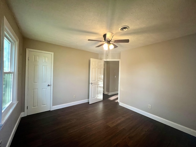unfurnished bedroom featuring baseboards, dark wood-style flooring, multiple windows, and visible vents