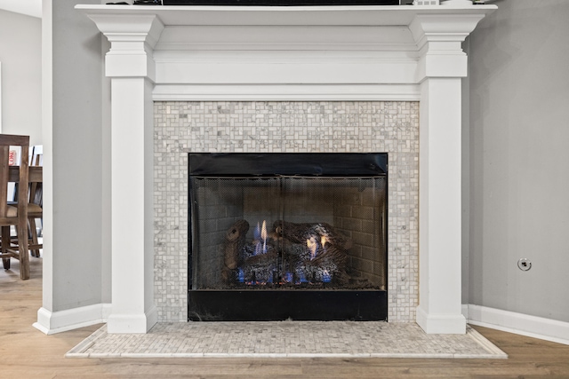 details with a tiled fireplace, baseboards, and wood finished floors