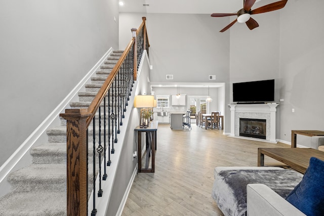 living area with baseboards, light wood finished floors, a high ceiling, and a ceiling fan