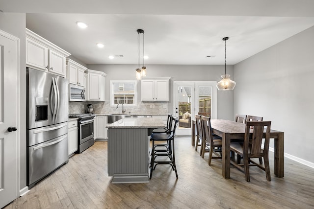 kitchen with light wood-type flooring, appliances with stainless steel finishes, decorative backsplash, and a kitchen island