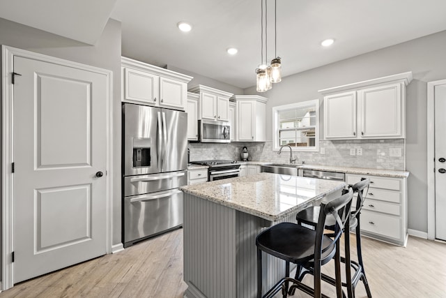 kitchen with light stone counters, a kitchen island, decorative backsplash, stainless steel appliances, and light wood finished floors