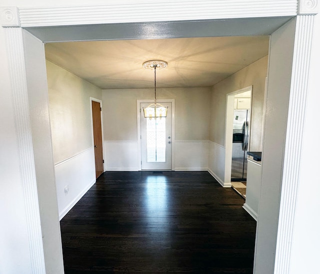 unfurnished dining area featuring an inviting chandelier, a wainscoted wall, and dark wood-style floors