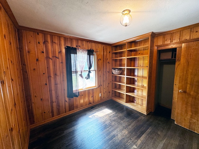 unfurnished room with wooden walls, wood finished floors, a textured ceiling, baseboards, and visible vents