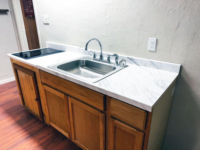 kitchen with light countertops, a sink, dark wood-style floors, brown cabinetry, and a textured wall