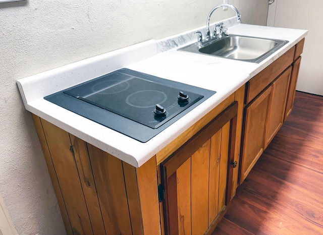 kitchen with light countertops, a sink, brown cabinets, dark wood-style floors, and black electric cooktop