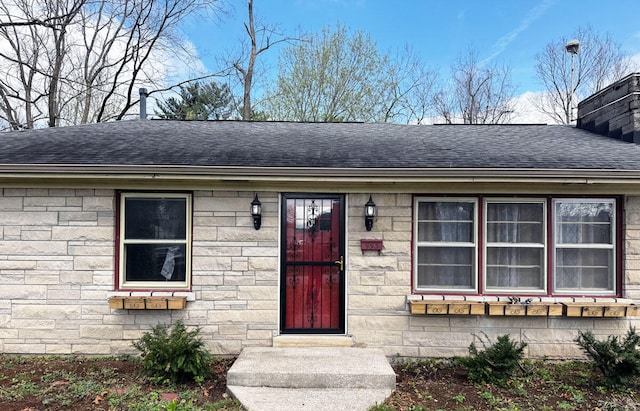 doorway to property featuring stone siding and roof with shingles