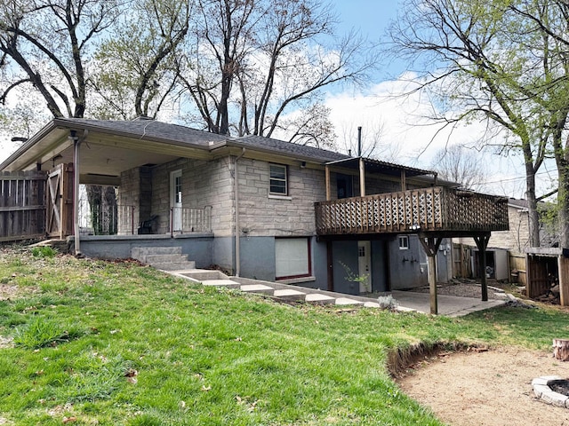 rear view of property featuring stone siding, fence, a wooden deck, a lawn, and a patio area