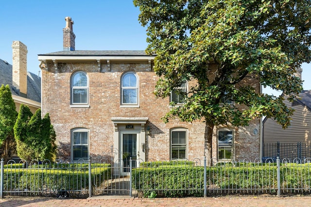 italianate home featuring brick siding, a fenced front yard, and a chimney