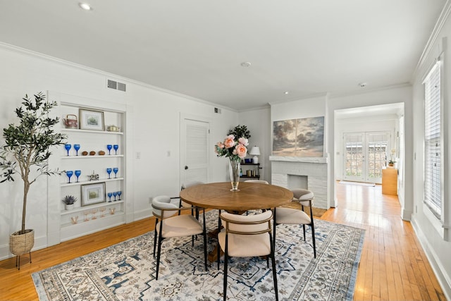 dining space with visible vents, baseboards, a fireplace, ornamental molding, and light wood-type flooring