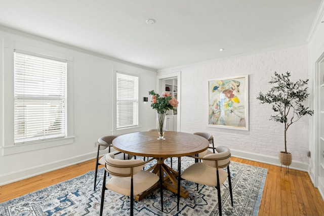 dining area featuring baseboards, ornamental molding, light wood-style flooring, and brick wall