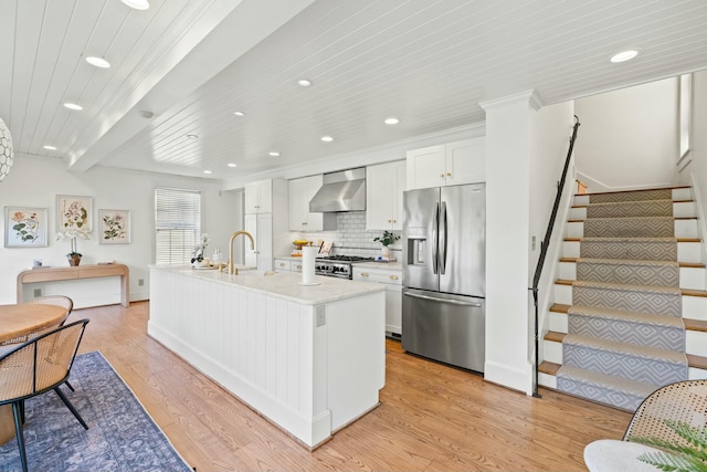 kitchen with light wood-style flooring, decorative backsplash, white cabinets, appliances with stainless steel finishes, and wall chimney exhaust hood