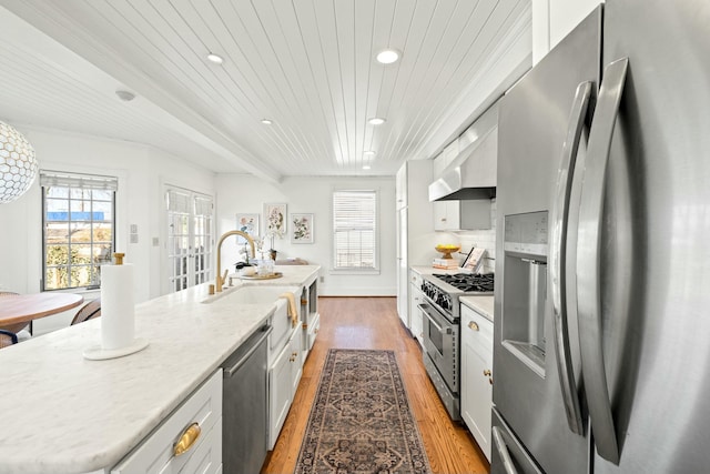 kitchen featuring light wood-type flooring, a center island with sink, a sink, extractor fan, and appliances with stainless steel finishes