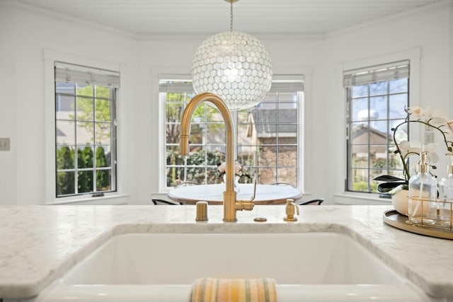 interior details with light stone countertops, a sink, decorative light fixtures, and crown molding