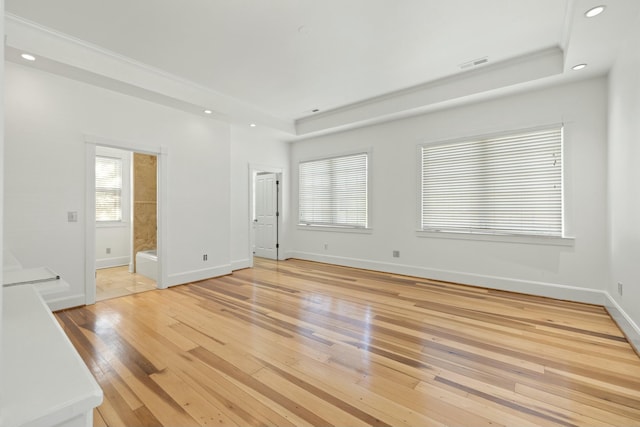 empty room featuring a raised ceiling, light wood-type flooring, baseboards, visible vents, and recessed lighting