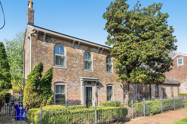 italianate home with brick siding, fence, and a chimney