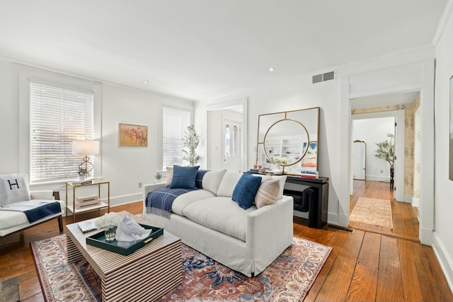 living area with baseboards, visible vents, crown molding, and hardwood / wood-style flooring