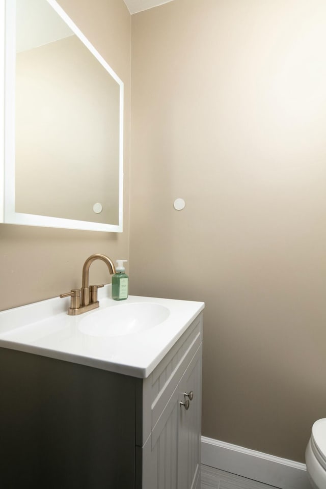 half bathroom with toilet, baseboards, and vanity