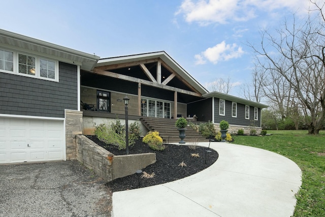 view of front of house featuring a front yard, an attached garage, stone siding, covered porch, and driveway