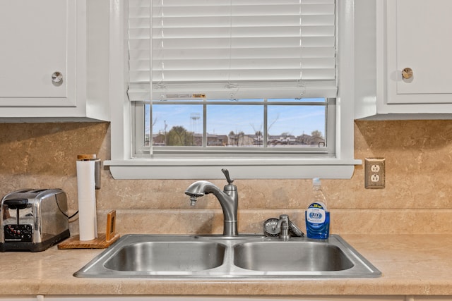 room details with a sink, light countertops, decorative backsplash, and white cabinetry