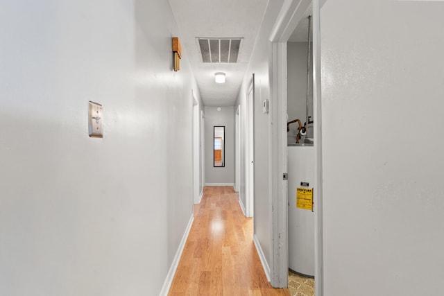 hallway with light wood-type flooring, baseboards, visible vents, and water heater