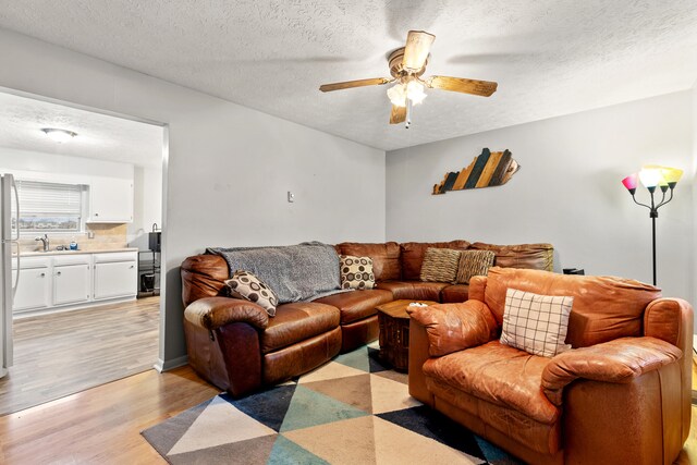 living room featuring ceiling fan, light wood-type flooring, and a textured ceiling