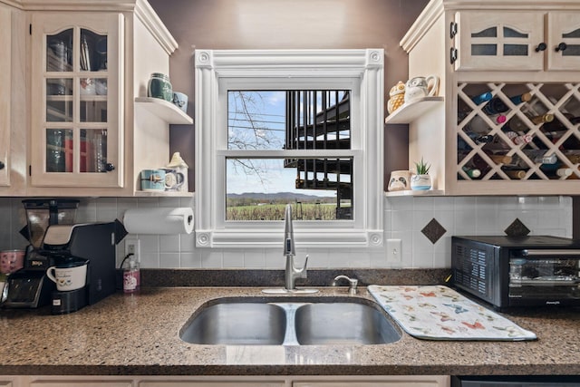 kitchen featuring glass insert cabinets, backsplash, a sink, and open shelves