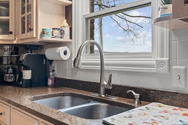 kitchen with dark stone countertops, decorative backsplash, glass insert cabinets, and a sink