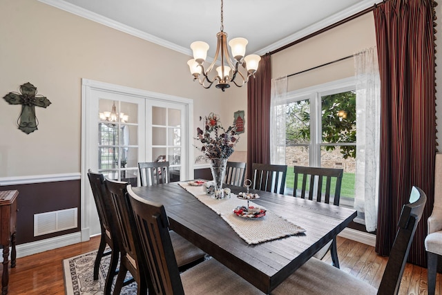 dining room featuring wood finished floors, ornamental molding, baseboards, visible vents, and a notable chandelier