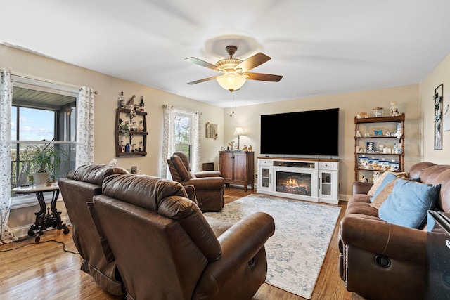living room featuring a glass covered fireplace, ceiling fan, wood finished floors, and baseboards