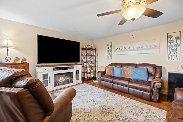 living area with wood finished floors, a ceiling fan, and a glass covered fireplace