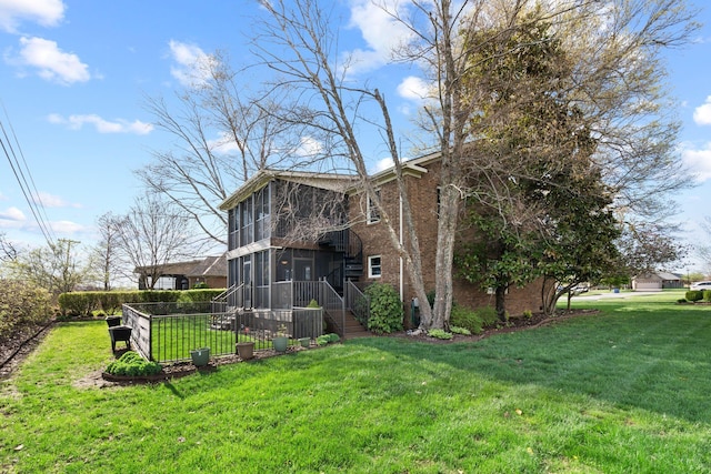view of side of home with a sunroom, fence, a lawn, and brick siding