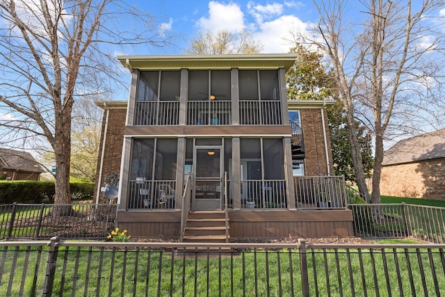 back of property with a lawn, a fenced front yard, brick siding, and a sunroom