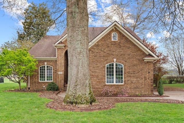 view of home's exterior featuring brick siding, roof with shingles, and a lawn
