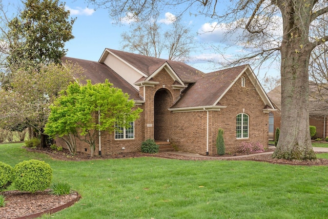 view of front of home with roof with shingles, a front lawn, and brick siding