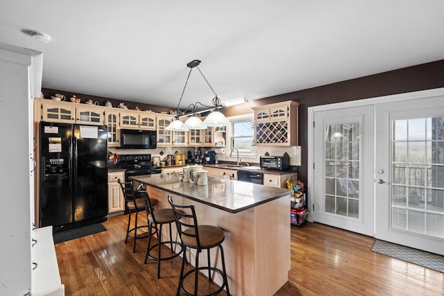 kitchen with black appliances, dark countertops, a kitchen breakfast bar, and dark wood-type flooring