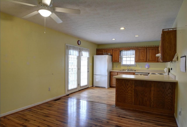 kitchen with a peninsula, freestanding refrigerator, light wood-style floors, range with electric cooktop, and a sink