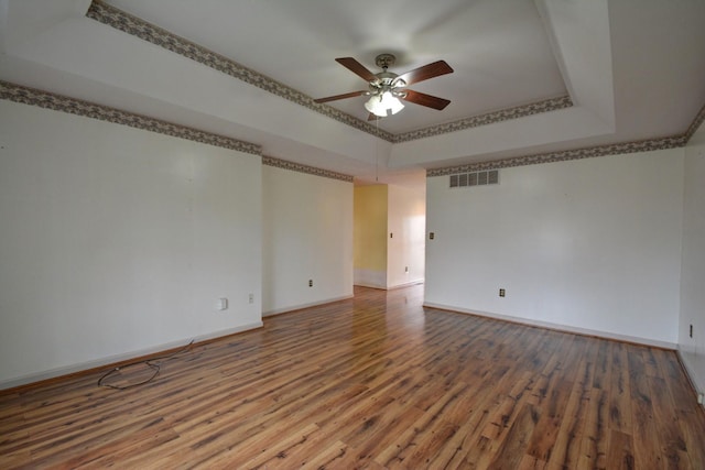 empty room featuring visible vents, ceiling fan, a tray ceiling, and wood finished floors