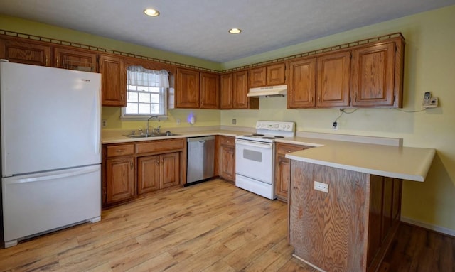 kitchen featuring white appliances, a peninsula, under cabinet range hood, brown cabinets, and a sink