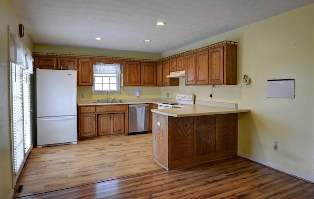 kitchen with white appliances, a peninsula, under cabinet range hood, a sink, and brown cabinets