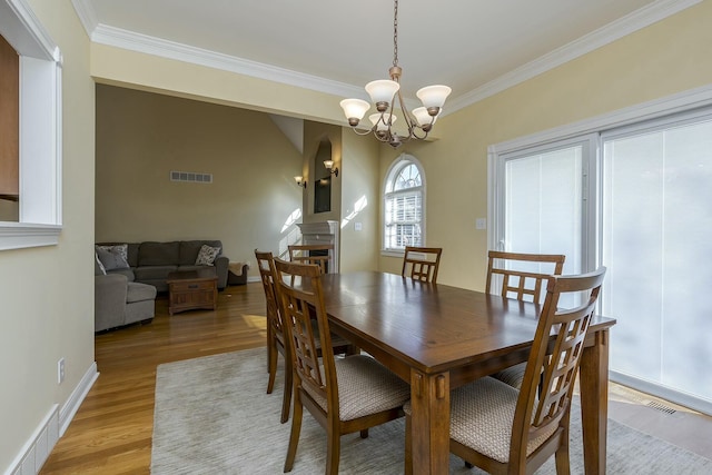 dining room with crown molding, visible vents, light wood-style flooring, and a notable chandelier