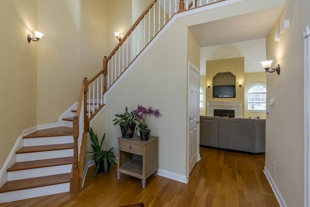 stairs with baseboards, a lit fireplace, and wood finished floors