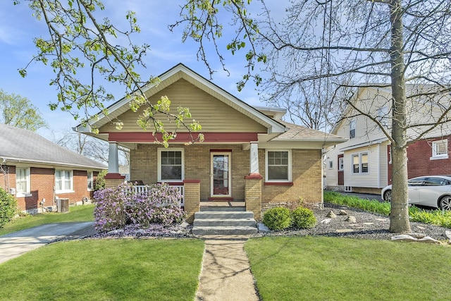 bungalow-style home featuring a front yard, brick siding, central air condition unit, and covered porch