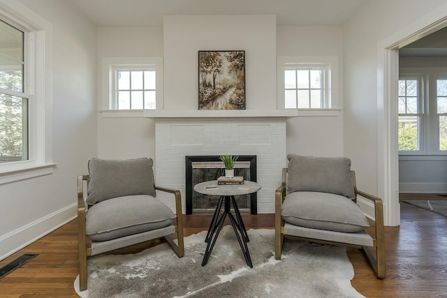 sitting room featuring wood finished floors, visible vents, baseboards, and a brick fireplace