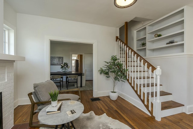 staircase with visible vents, a brick fireplace, wood finished floors, and a healthy amount of sunlight