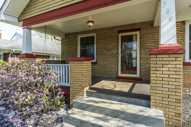 doorway to property featuring brick siding and a porch