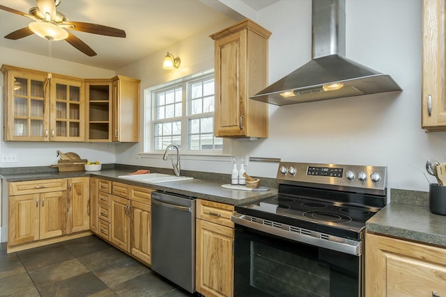 kitchen featuring wall chimney exhaust hood, a sink, ceiling fan, appliances with stainless steel finishes, and dark countertops
