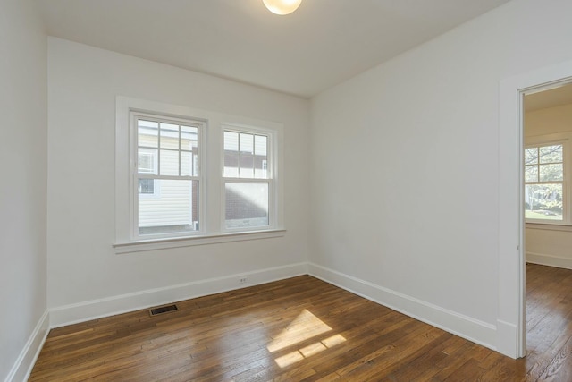 unfurnished room with visible vents, dark wood-style flooring, and baseboards