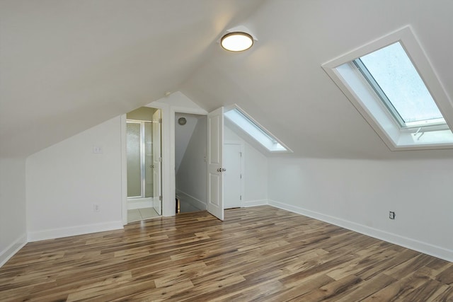 additional living space with baseboards, lofted ceiling with skylight, and wood finished floors