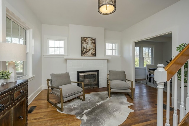 sitting room with a fireplace, visible vents, baseboards, and wood finished floors
